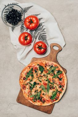 Delicious pizza on wooden cutting board and tomatoes on light background clipart