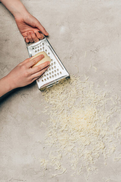 Close-up view of woman grating cheese on light background