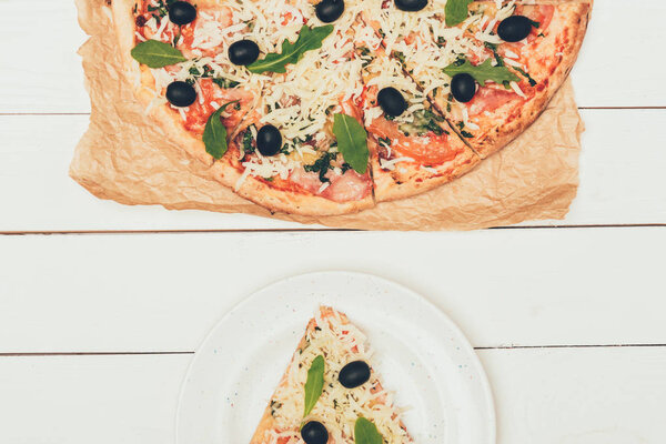Pizza slice and whole pizza on white wooden background