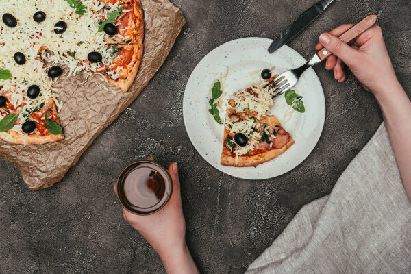 Close-up view of woman having dinner with pizza and drink on dark background