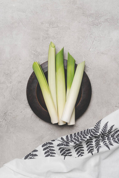 top view of fresh healthy leeks on plate and napkin on grey