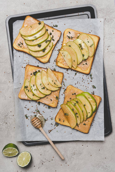 healthy sandwiches with slices of apple, lime and honey dipper on grey  