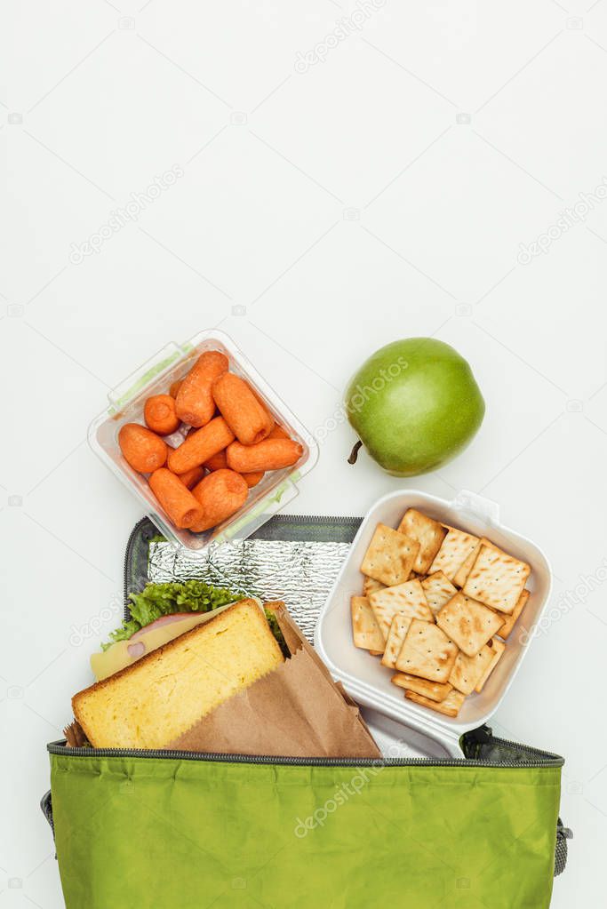 top view of sandwich and carrots with apple in lunch bag isolated on white
