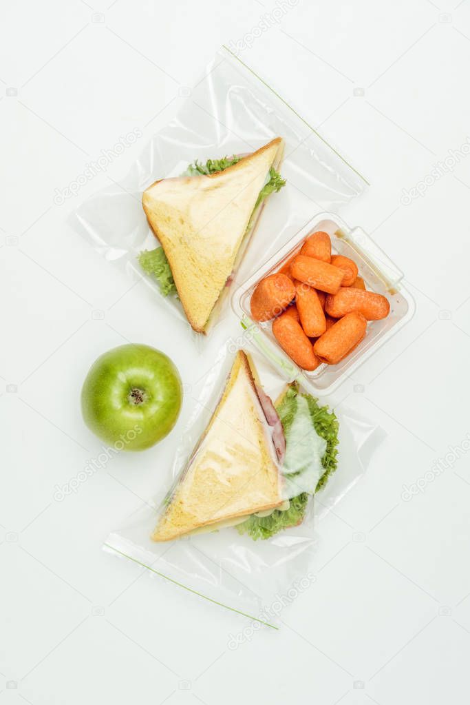 top view of sandwiches in ziplock bags and carrots in lunch box isolated on white