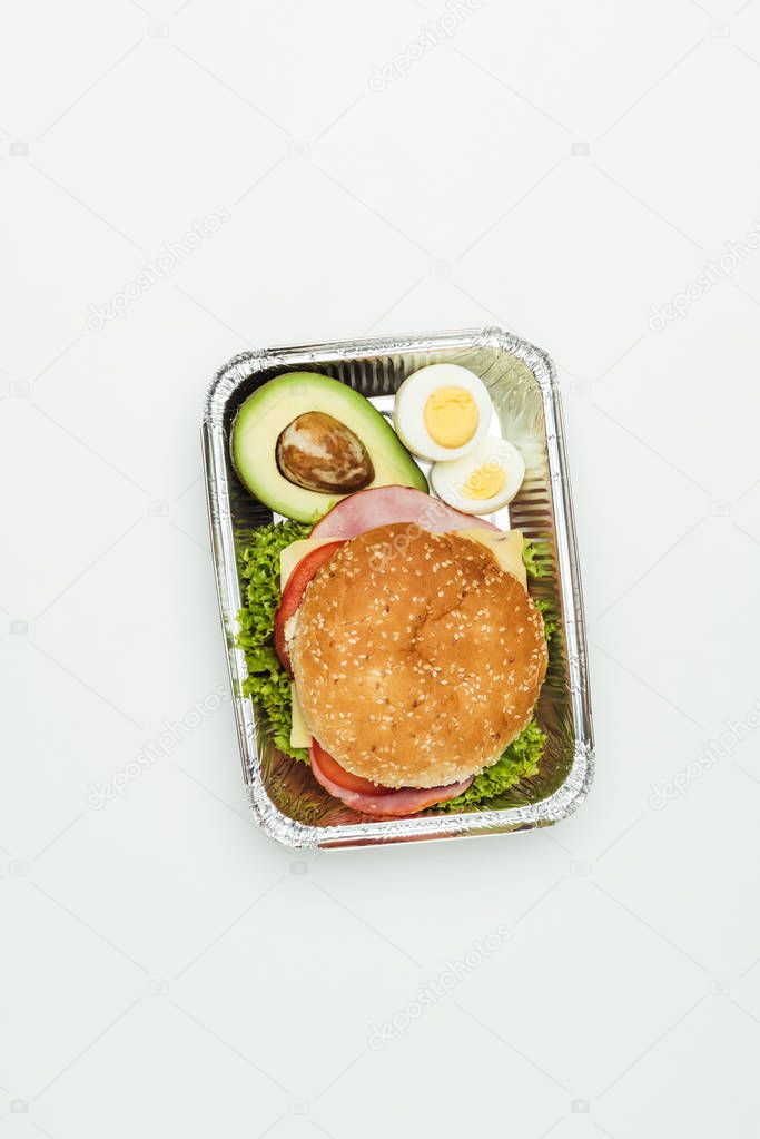 top view of burger with avocado and eggs in lunch box isolated on white