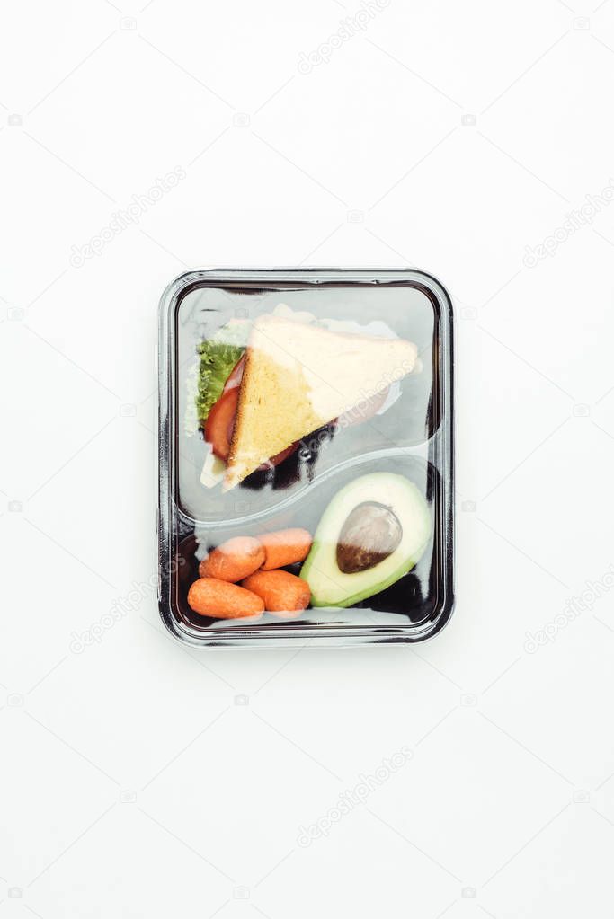 top view of closed plastic lunch box with sandwich and vegetables isolated on white