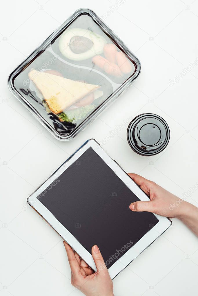 cropped image of woman holding tablet at table with food in lunch box isolated on white