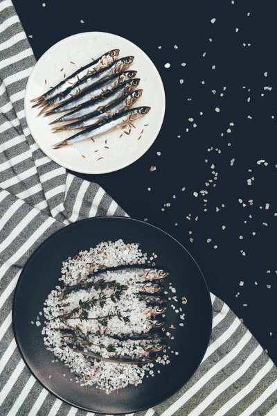 Top view of plate and frying pan with salted pile of fish and towel isolated on black