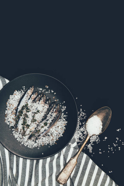 Frying pan with salted pile of fish, rosemary , spoon and towel isolated on black 