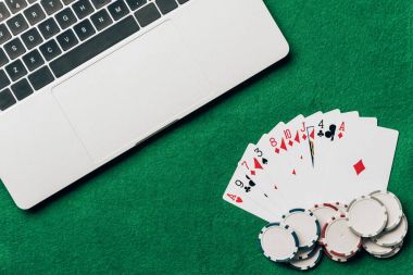 Playing cards and chips on casino table by laptop clipart