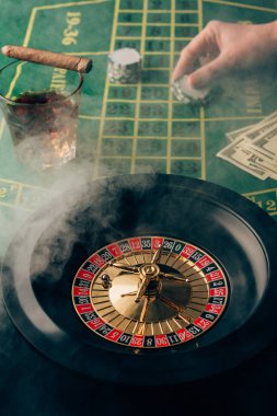 Smoke over female hand placing a bet on table with roulette clipart