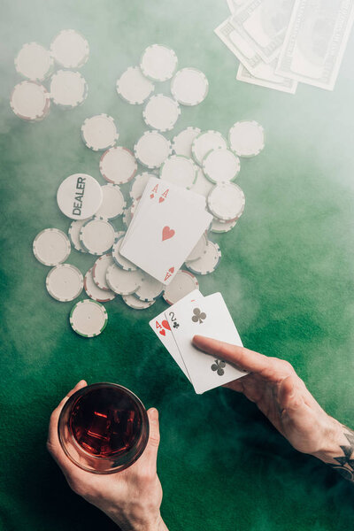 Man with whiskey and poker cards by casino table