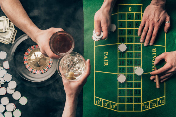 Люди тосты напитки во время игры в рулетку за столом казино
