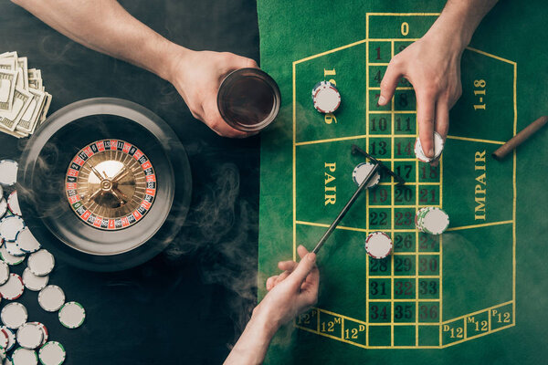 Дым над людьми, делающими ставки во время игры в рулетку на столе казино
