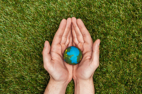 cropped image of man holding earth model in hands above green grass, earth day concept