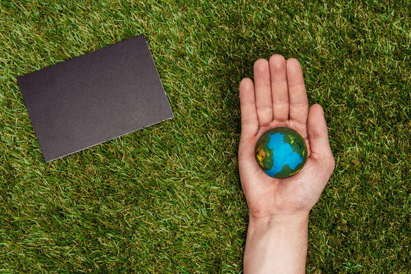 cropped image of man holding earth model on hand, blackboard on green grass, earth day concept