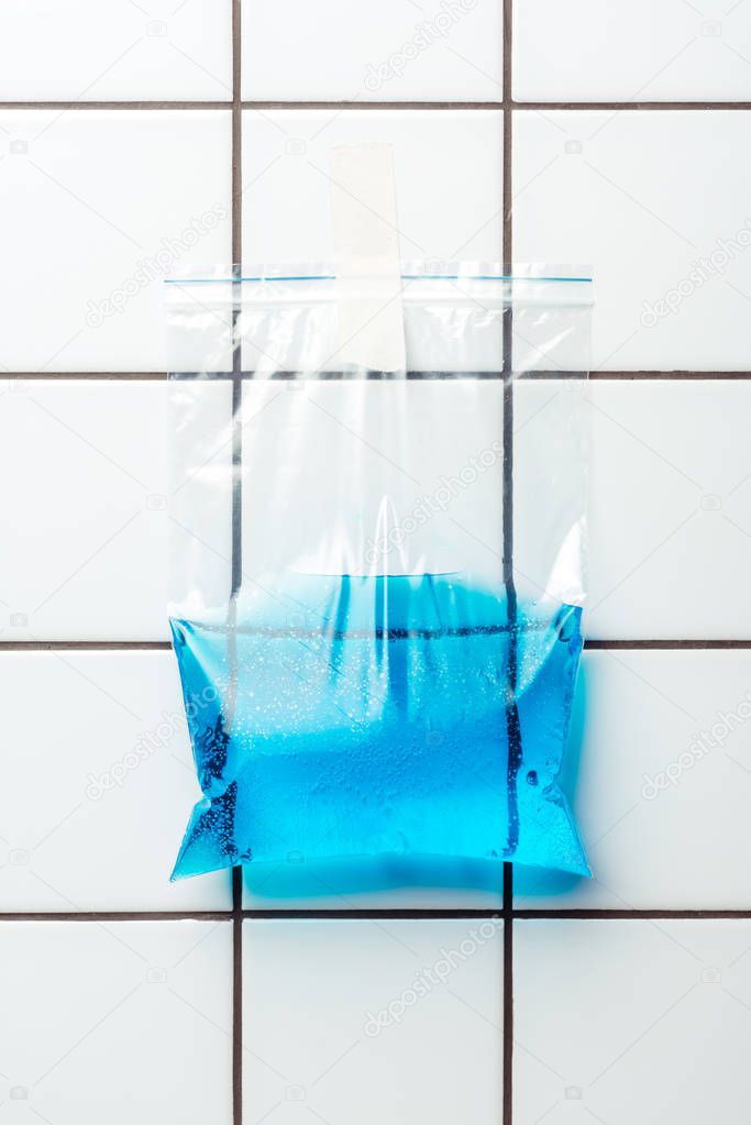 ziplock plastic bag with blue water hanging on tile wall, earth day concept