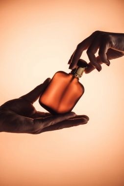 cropped view of male and female hands with bottle of perfume, isolated on orange  clipart