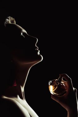 silhouette of sensual woman spraying perfume on neck, isolated on black clipart