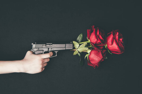 Woman shooting gun with red roses isolated on black