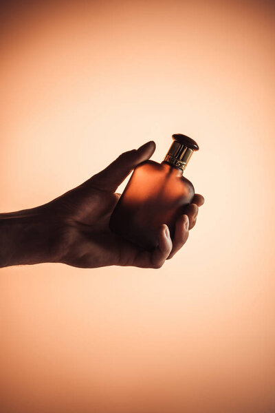 cropped view of male hand with perfume, isolated on orange