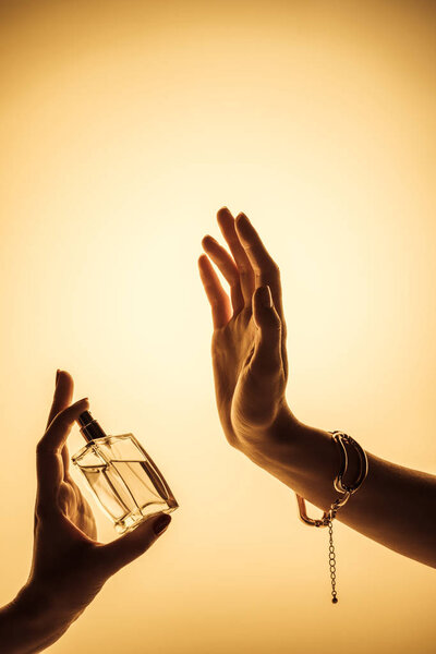 cropped view of woman spraying perfume on hand to feel fragrance, isolated on yellow