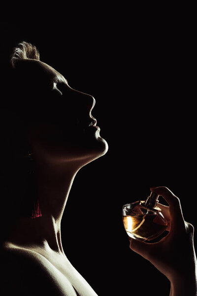 silhouette of sensual woman spraying perfume on neck, isolated on black