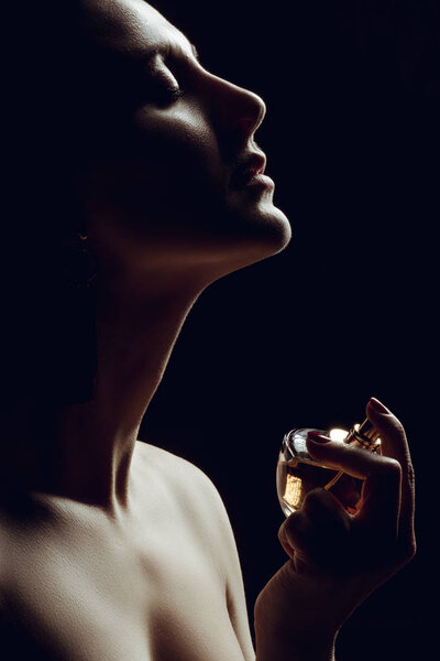 silhouette of sensual girl spraying perfume on neck, isolated on black