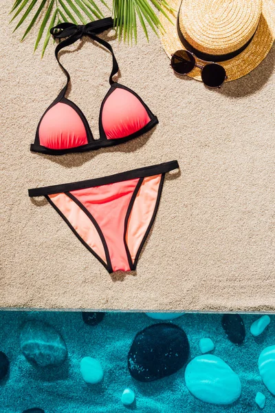 top view of stylish pink bikini with accessories on sandy beach