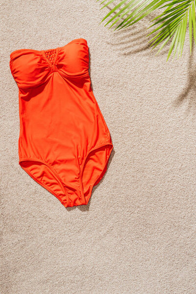 top view of stylish red swimsuit on sandy beach