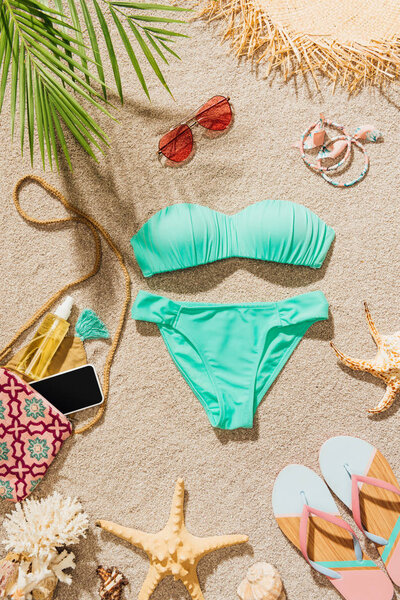 top view of beautiful bikini and various accessories lying on sandy beach