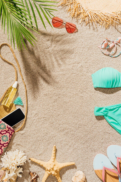 top view of bikini and various accessories lying on sandy beach