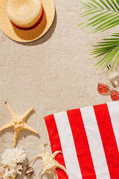 top view of striped towel with straw hat and sunglasses on sandy beach