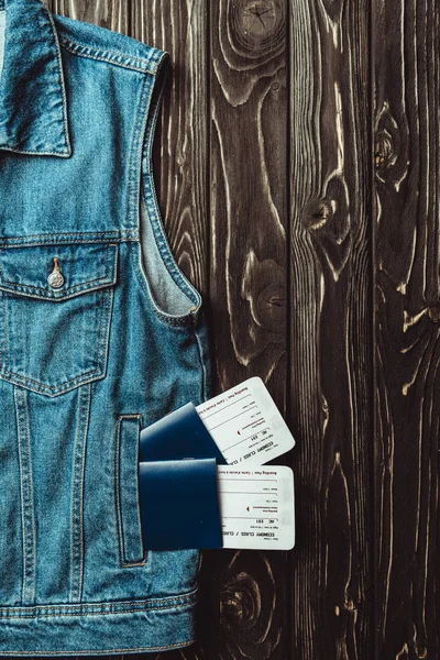 flat lay with denim vest, passports and tickets on dark wooden surface