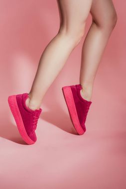 cropped image of girl in stylish sneakers standing on toes on pink background clipart