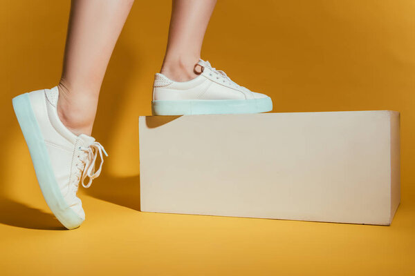 cropped image of woman feet in stylish sneakers on yellow background