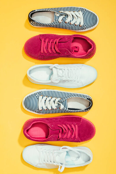 top view of different stylish female sneakers placed in row on yellow background