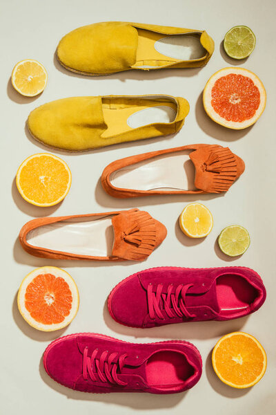top view of stylish female shoes placed in row surrounded by slices of different citrus fruits on white background