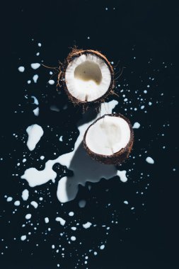 top view of halved organic coconut and coconut milk on black clipart