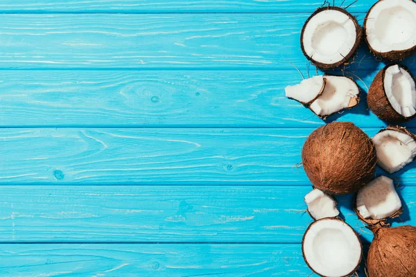 top view of whole coconuts and pieces on turquoise wooden surface