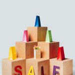 Colored shopping bags on wooden stands with sale sign isolated on white, summer sale concept