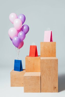 bundle of pink and violet balloons near paper bags on stands, summer sale concept clipart