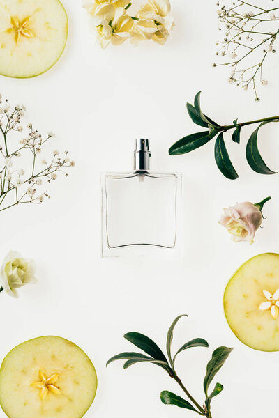 top view of bottle of perfume surrounded with flowers and apple slices isolated on white