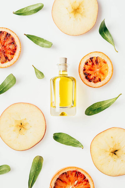 top view of bottle of perfume with slices of fruits and green leaves around on white