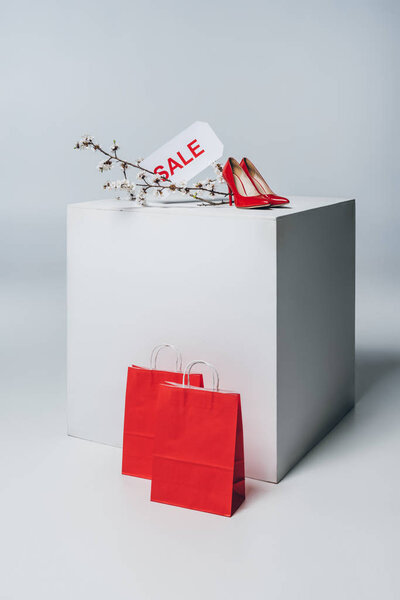 red high heels with sale sign on white cube, summer sale concept