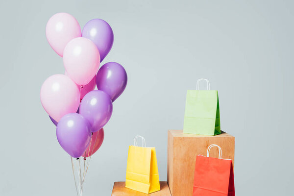 bundle of pink and violet balloons near shopping bags on stands isolated on white, summer sale concept