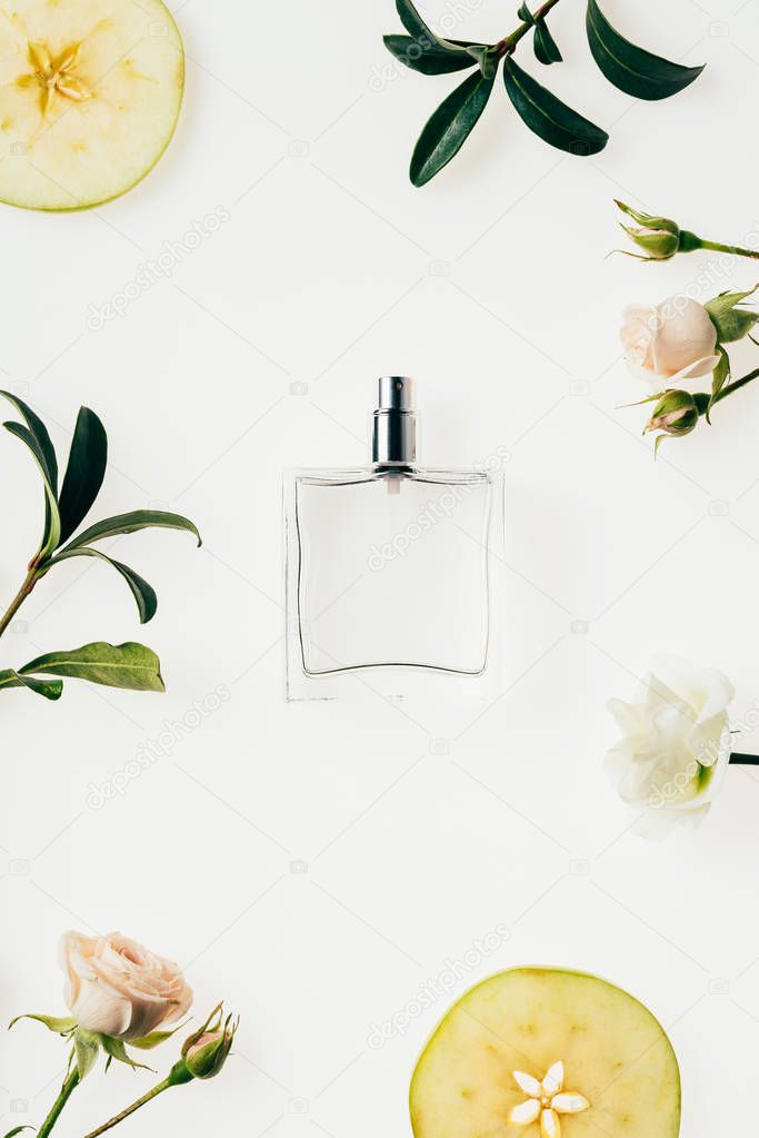 top view of glass bottle of perfume surrounded with flowers and apple slices isolated on white