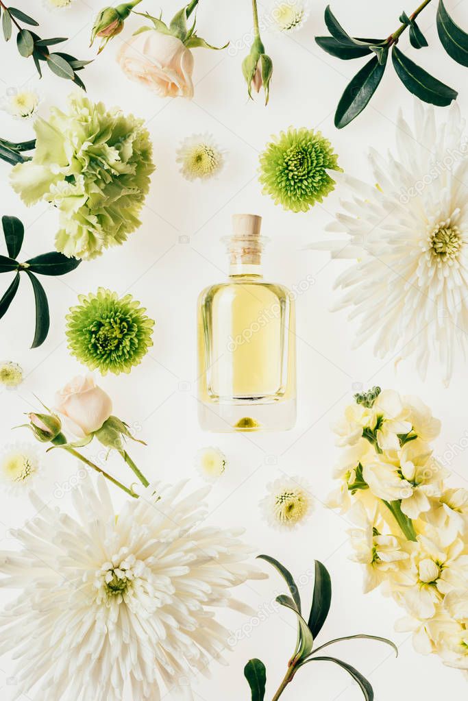 top view of bottle of aromatic perfume surrounded with flowers and green branches isolated on white