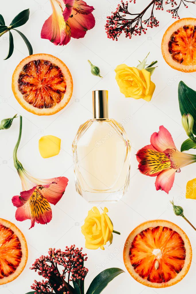 top view of bottle of aromatic perfume surrounded with flowers and blood orange slices isolated on white