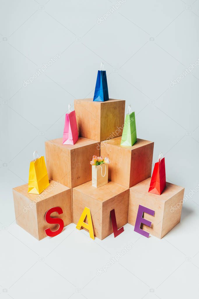 high angle view of colored shopping bags on wooden stands with sale sign, summer sale concept